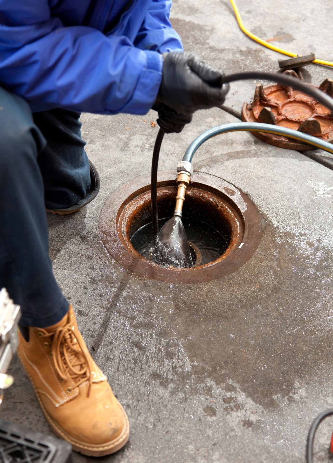 Technician hydro jetting a sewer line through a manhole